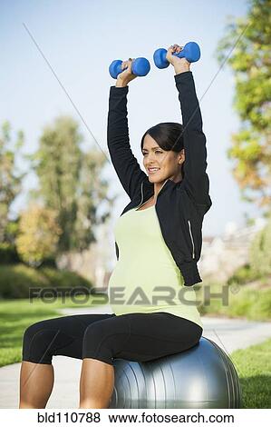 Stock Photo - Pregnant Hispanic woman lifting weights outdoors. Fotosearch