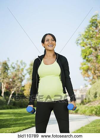 Stock Photo - Pregnant Hispanic woman lifting weights outdoors. Fotosearch