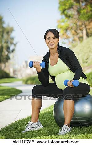 Stock Photograph - Pregnant Hispanic woman lifting weights outdoors. Fotosearch