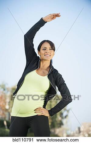 Stock Image - Pregnant Hispanic woman stretching outdoors. Fotosearch