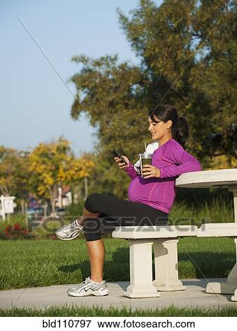 Stock Photo - Pregnant Hispanic woman using cell phone. Fotosearch