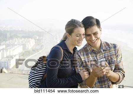 Picture - Smiling couple using cell phone outdoors. Fotosearch