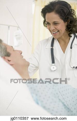 Stock Photo - Female doctor talking to a male patient lying in bed. Fotosearch