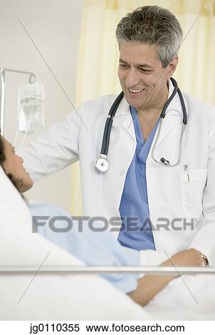 Stock Photography - Male doctor sitting next to a female patient lying in bed. Fotosearch