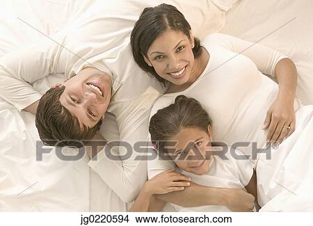 Picture - Young couple and their child lying together in bed looking up. Fotosearch