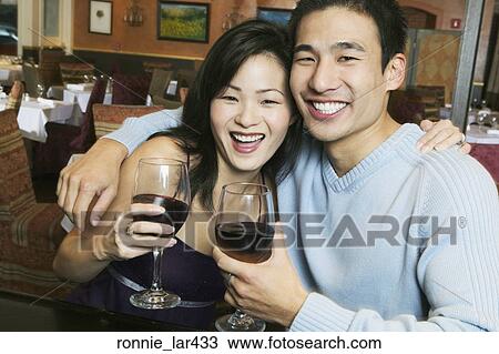 Stock Image - Portrait of a young couple smiling and holding wineglasses at a bar counter. Fotosearch