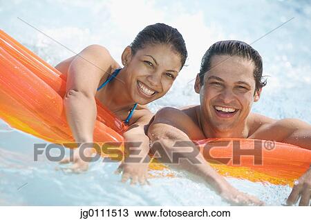 Stock Image - Young couple resting on an air mattress in a swimming pool. Fotosearch
