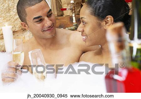 Stock Photography - Young couple together in a bubble bath holding glasses of champagne. Fotosearch