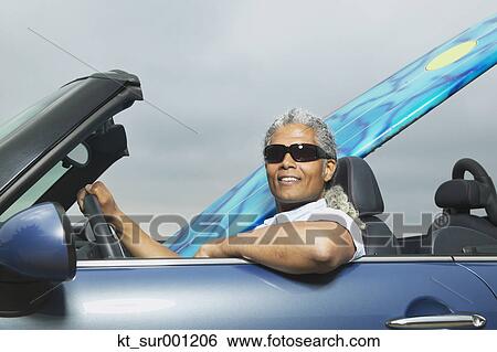 Stock Photograph - Senior man driving a convertible with a surfboard in it, Oakland, California, United States. Fotosearch