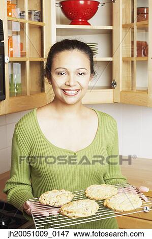 Stock Photo - Young woman holding a rack of baked goods. Fotosearch