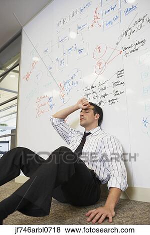 Stock Photo - Tired businessman sitting on floor leaning against whiteboard wall. Fotosearch
