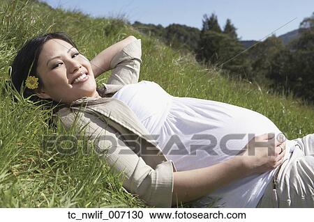 Stock Image - Pregnant Asian woman laying in the grass. Fotosearch