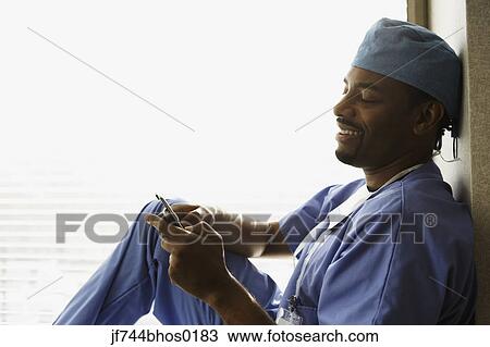 African male surgeon sitting in window alcove with cell phone View Large Photo Image Stock Image - African male surgeon sitting in window alcove with cell phone. Fotosearch