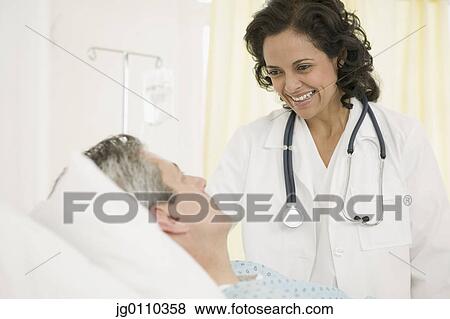 Stock Photo - Female doctor talking to a male patient lying in bed. Fotosearch
