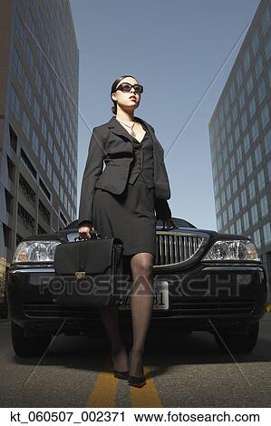 Stock Image - Asian businesswoman with briefcase standing at front of car. Fotosearch