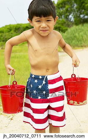 Stock Image - Young boy carrying two buckets at the beach. Fotosearch