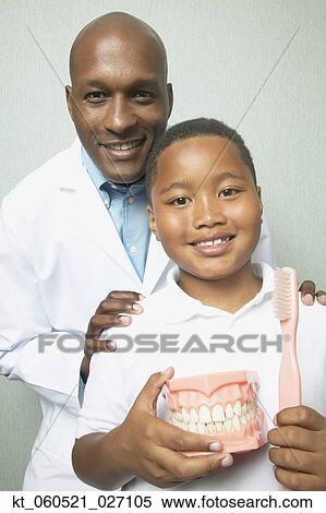 Stock Photography - African male dentist with boys holding toothbrush and model of teeth. Fotosearch