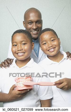 African male dentist with twin boys holding toothbrush and model of teeth View Large Photo Image Stock Photo - African male dentist with twin boys holding toothbrush and model of teeth. Fotosearch
