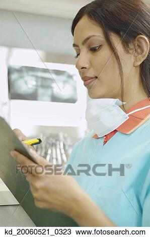 Stock Image - Indian female dental assistant writing on chart. Fotosearch