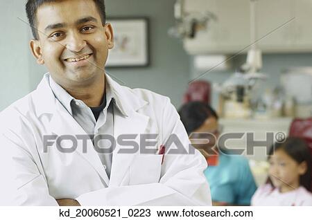 Indian male dentist with assistant and patient in background View Large Photo Image Stock Image - Indian male dentist with assistant and patient in background. Fotosearch