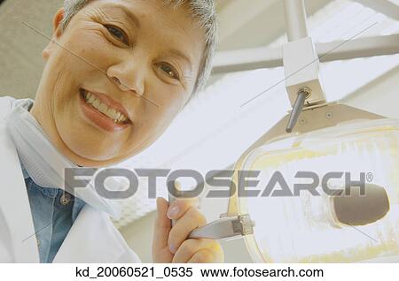 Stock Photography - Senior Asian female dentist adjusting light. Fotosearch