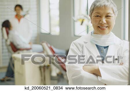 Senior Asian female dentist with assistant and patient in background View Large Photo Image Picture - Senior Asian female dentist with assistant and patient in background. Fotosearch