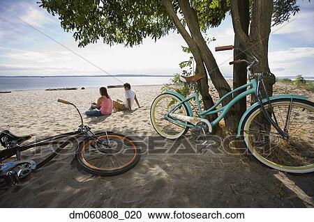 Couple sitting on beach with bicycles View Large Photo Image Stock Image - Couple sitting on beach with bicycles. Fotosearch