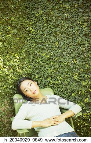 Stock Photo - High angle view of a young woman sitting on a chair outdoors. Fotosearch