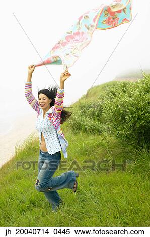 Young woman standing in a field holding a scarf above her head View Large Photo Image Stock Photography - Young woman standing in a field holding a scarf above her head. Fotosearch