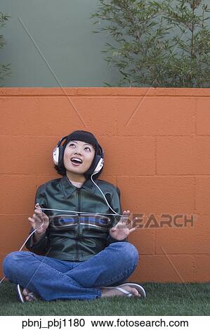 Stock Image - Young Asian woman listening to headphones outdoors. Fotosearch