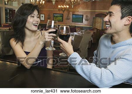 Stock Image - Young couple toasting glasses of wine at a bar counter. Fotosearch