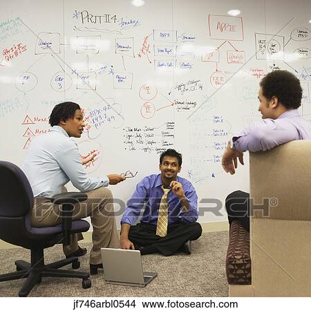 Picture - Businesspeople having a meeting in front of a whiteboard wall. Fotosearch