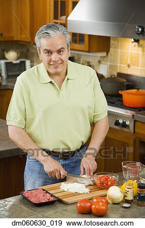 Stock Photo - Hispanic man chopping vegetables in kitchen. Fotosearch