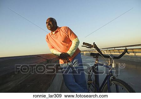Mature man leaning against railing on a bridge View Large Photo Image Stock Photo - Mature man leaning against railing on a bridge. Fotosearch