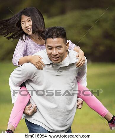 Picture - Asian father carrying daughter outdoors. Fotosearch