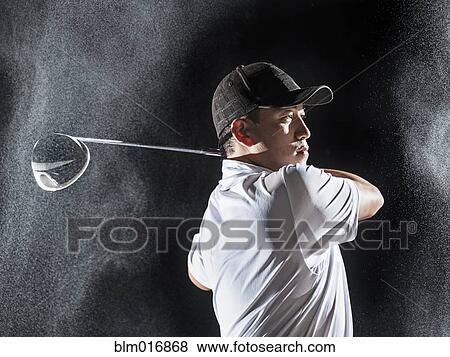 Stock Photo - Asian golf player swinging club in rain. Fotosearch