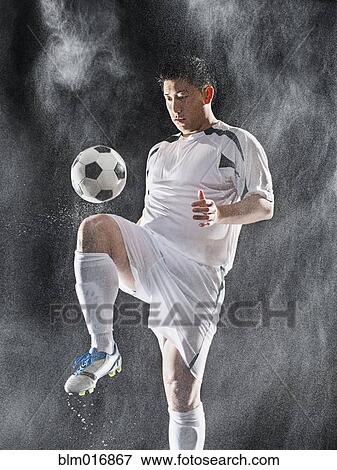 Stock Photo - Asian soccer player kicking ball in rain. Fotosearch