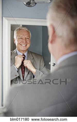 Stock Image - Businessman adjusting his tie in mirror. Fotosearch