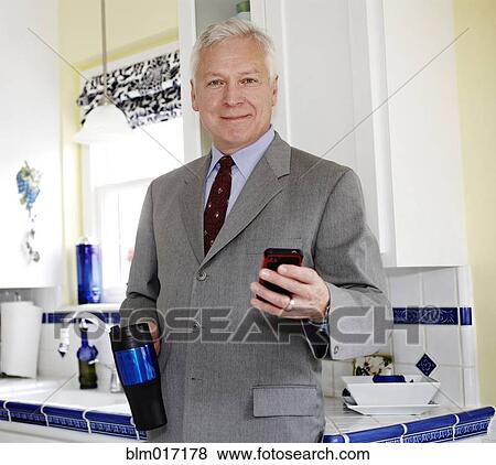 Stock Photo - Businessman using cell phone in kitchen. Fotosearch
