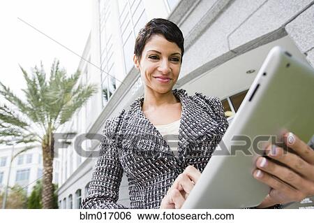 Stock Photograph - Cape Verdean businesswoman using tablet computer outdoors. Fotosearch