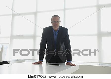 Stock Image - Caucasian businessman leaning over desk. Fotosearch
