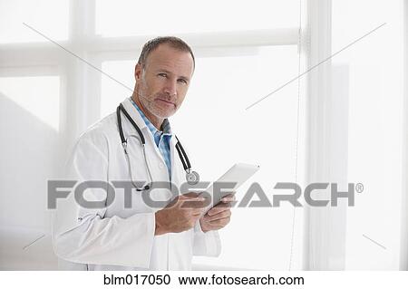 Stock Image - Caucasian doctor holding tablet computer in office. Fotosearch