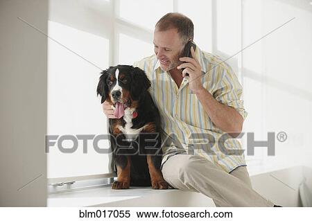 Stock Photography - Caucasian man hugging dog and talking on cell phone. Fotosearch