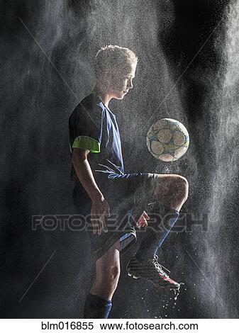 Stock Photography - Caucasian soccer player kicking ball in rain. Fotosearch