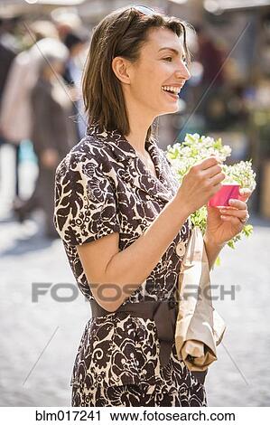 Stock Image - Caucasian woman eating ice cream on city street. Fotosearch