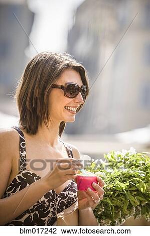 Stock Image - Caucasian woman eating ice cream on city street. Fotosearch