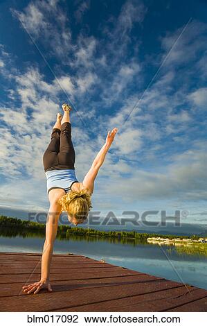 Stock Image - Caucasian woman practicing yoga on dock on still lake, Anchorage, Alaska, United States. Fotosearch