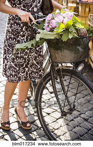 Picture - Caucasian woman pushing bicycle with flowers. Fotosearch