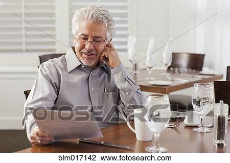 Stock Image - Hispanic businessman reading papers in cafe. Fotosearch