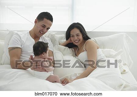 Stock Image - Hispanic family relaxing in bed. Fotosearch
